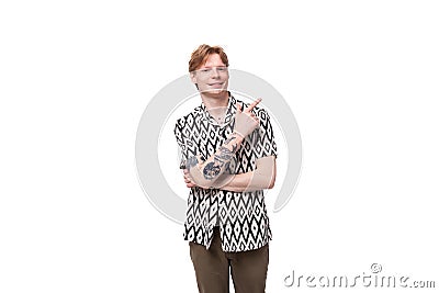 young red-haired man in a summer shirt with a rhombus print points with his hand on a background with copy space Stock Photo