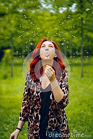 Young red-haired woman blows away a dandelion. Stock Photo