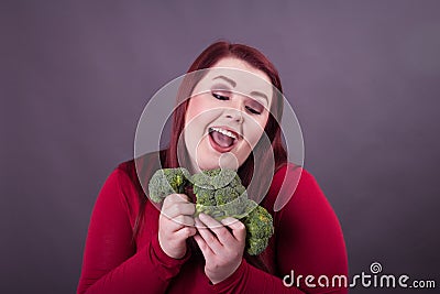 Young red head woman looking at and holding broccoli florets Stock Photo