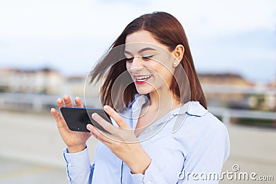 Young redhead businesswoman messaging on smartphone and laughing at outdoors Stock Photo