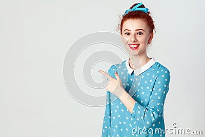 Young redhead caucasian girl with hair bun pointing her index finger away, indicating copy space on white blank wall for your cont Stock Photo