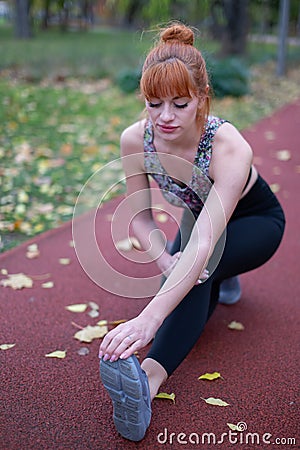 Young redhead woman leg stretching warm up before running on track at autumn Stock Photo