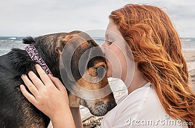 Young red haired girl kissing head of pet Huntaway dog, New Zealand Stock Photo