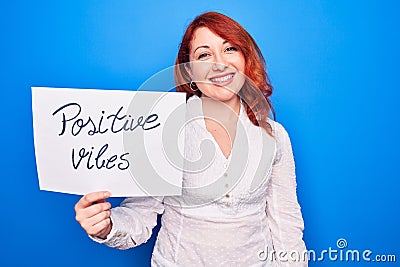 Young redhead woman asking for optimist attitude holding paper with positive vibes message looking positive and happy standing and Stock Photo