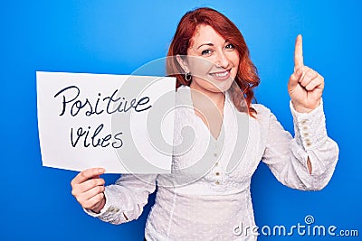 Young redhead woman asking for optimist attitude holding paper with positive vibes message smiling with an idea or question Stock Photo