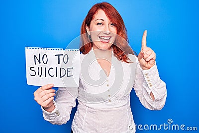 Young redhead woman asking for stop depression holding paper with not to suicide message smiling with an idea or question pointing Stock Photo