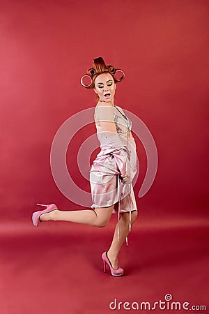 Young redhead woman with hair curlers dressed in neglige, peignoir, dressing gown posing on a burgundy background Stock Photo