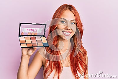 Young redhead woman holding makeup nudes looking positive and happy standing and smiling with a confident smile showing teeth Stock Photo