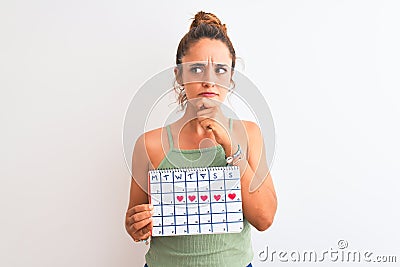 Young redhead woman holding menstruation calendar over isolated background serious face thinking about question, very confused Stock Photo