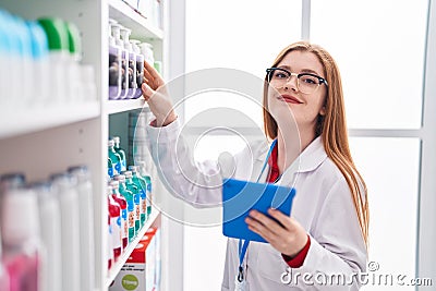 Young redhead woman pharmacist using touchpad working at pharmacy Stock Photo