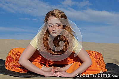 Young redhead woman sitting in purna titli yoga pose on the beach Stock Photo