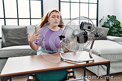 Young redhead woman using electric ventilator at home Stock Photo