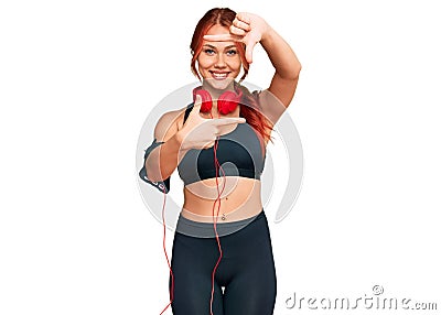 Young redhead woman wearing gym clothes and using headphones smiling making frame with hands and fingers with happy face Stock Photo