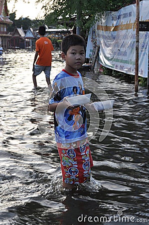 A young refugee boy is bringing food in a flooded street of Bangkok, Thailand, on 31 October 2011 Editorial Stock Photo
