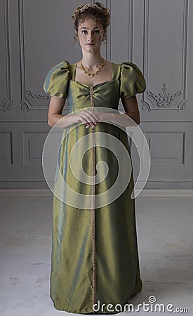 A young Regency woman wearing a green shot silk dress and standing in front of a white paneled wall Stock Photo