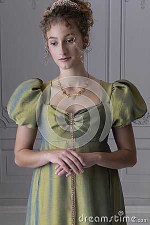 A young Regency woman wearing a green shot silk dress and standing in front of a white paneled wall Stock Photo