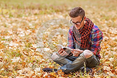 Young relaxed man reading book in nature, back on tree, meadow b Stock Photo