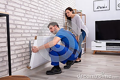 Repairman Installing Radiator On Brick Wall At Home Stock Photo