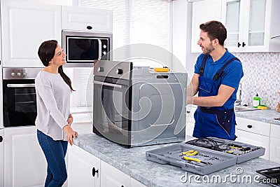 Young Repairman Repairing Oven On Kitchen Worktop Stock Photo