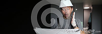 Young repairman standing in empty flat, looking at construction plan and feeling shocked Stock Photo