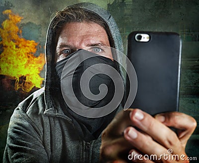 Young rioter filming street chaos . ultra and radical man masked recording riot video on mobile phone during violent turmoil Stock Photo