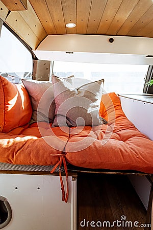 Young 30s caucasian woman with dark hair making the bed in a self converted minivan campervan for van life with lovely light Stock Photo