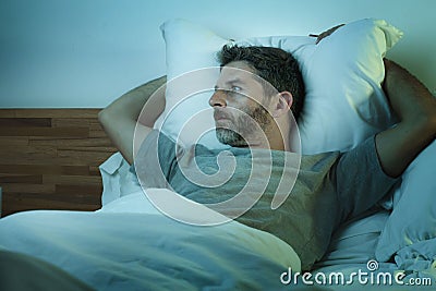 Young sad and depressed man lying thoughtful and pensive on bed looking away feeling lost thinking suffering some problem in Stock Photo