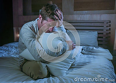 Young sad and desperate man awake late night on bed in darkness suffering depression and anxiety looking stressed crying alone hol Stock Photo