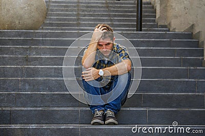 Young sad and desperate man sitting outdoors at street stairs suffering anxiety and depression feeling miserable crying in Stock Photo