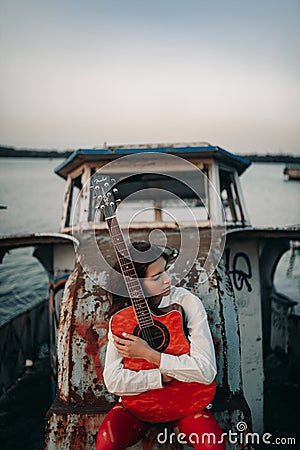 A young woman sits with guitar on old abandoned ship Stock Photo