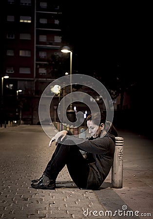 Young sad woman sitting on street ground at night alone desperate suffering depression left abandoned Stock Photo