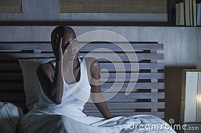 Young scared and stressed black african American woman depressed on bed upset unable to sleep suffering hangover headache feeling Stock Photo