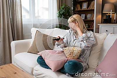 Young scared woman sitting alone at home on the floor watching scary horror movie on the television. Disgusted animal lover female Stock Photo