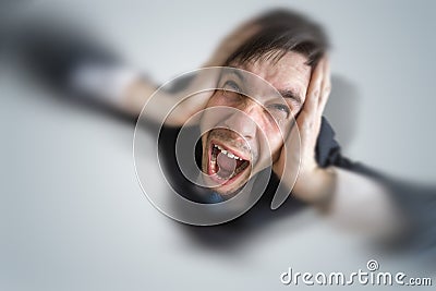 Young schizophrenic man suffers from headache and covering his ears with hands Stock Photo