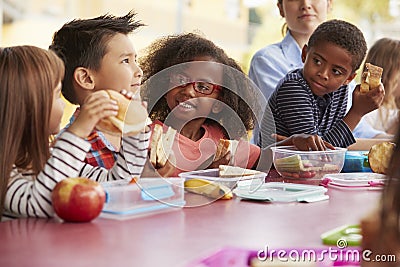 Young school kids eating lunch talking at a table together Stock Photo