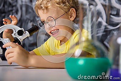 Boy in a yellow T-shirt looks at crystals on microscope stage in the laboratory Stock Photo