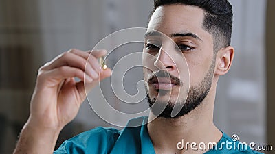 Young scientist hispanic man medical employee holding clear transparent capsule tablet in hand arabian doctor analysis Stock Photo