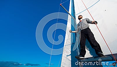 Young seaman on a sailboat standing on a sail boom. Captain of the yacht in the open sea. Stock Photo