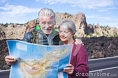 Young senior people enjoy travel and active lifestyle together - couple of old man and woman looking a map on the road - Stock Photo