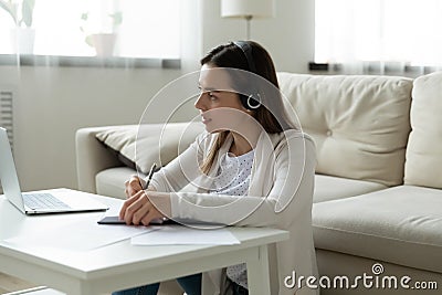 Focused woman in headphones watch webinar on laptop writing notes Stock Photo