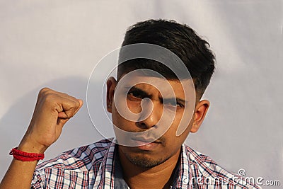 Young serious looking Indian man close up face portrait with fist up view on isolated dark background. Stock Photo