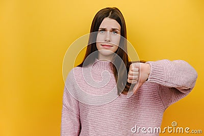 Young serious strict disappointed millennial woman show thumb down dislike gesture refusing say no, wearing pink knitted sweater Stock Photo