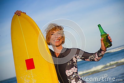 Young beautiful and happy surfer woman holding yellow surf board smiling cheerful drinking beer bottle enjoying summer holida Stock Photo