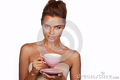 Young beautiful woman with dark hair picked up holding a ceramic cup and saucer pale pink drink tea or coffee on a white back Stock Photo