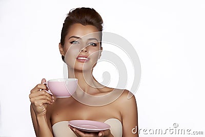 Young beautiful woman with dark hair picked up holding a ceramic cup and saucer pale pink drink tea or coffee on a white back Stock Photo