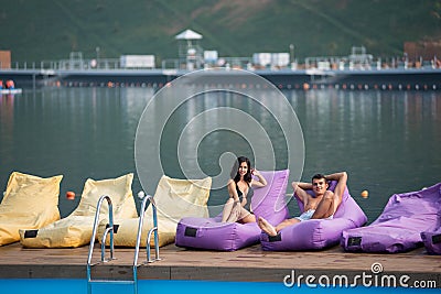 Young couple on cushioned loungers by swimming pool and lake on the background Stock Photo