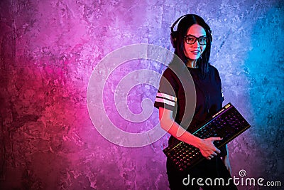 Young Disco Girl Wearing Gaming Headset Holding Gaming Keyboard. Room Lit in Retro, Retrowave or Cyberpunk Style Stock Photo