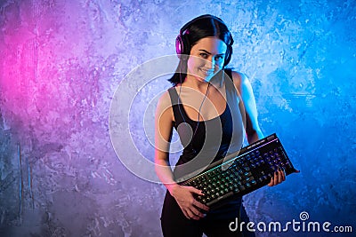 Young Disco Girl Wearing Gaming Headset Holding Gaming Kyeboard. Room Lit in Retro, Retrowave or Cyberpunk Style Stock Photo