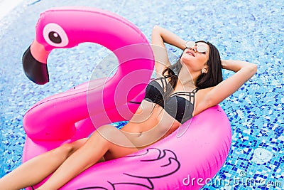 Young and girl having fun and laughing on an inflatable giant pink flamingo pool float mattress in a bikini. Attractive tanne Stock Photo