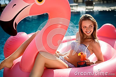 Young and girl having fun and laughing on an inflatable giant pink flamingo pool float mattress with a cocktail Stock Photo